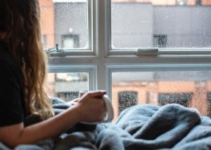 young woman staring out window during rain storm